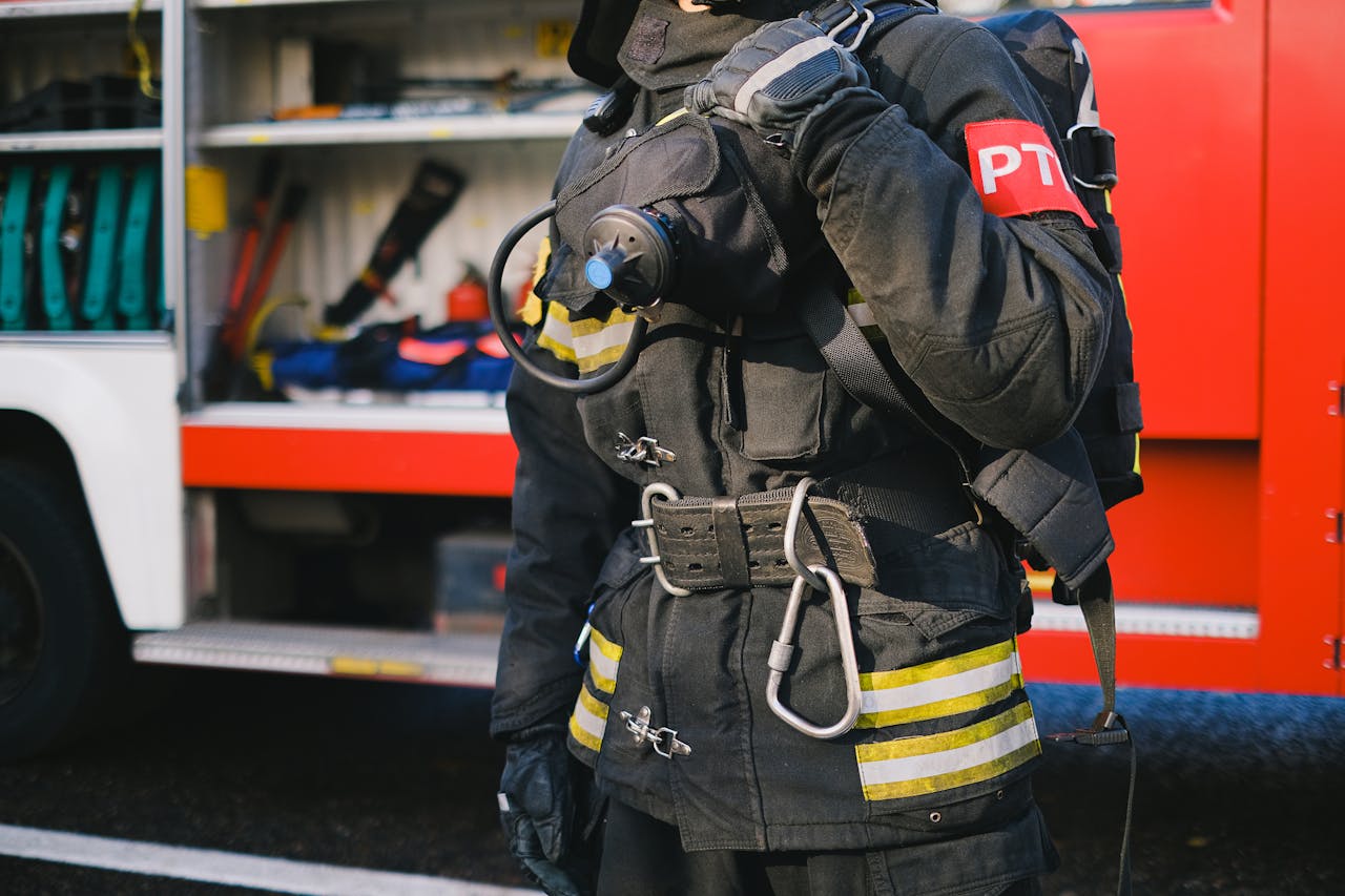 A firefighter wearing protective gear stands ready beside a fire truck, showcasing emergency preparedness.